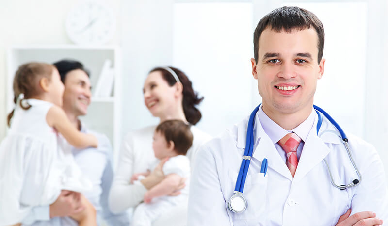 Doctor looks at camera with young family in background, disability and critical illness